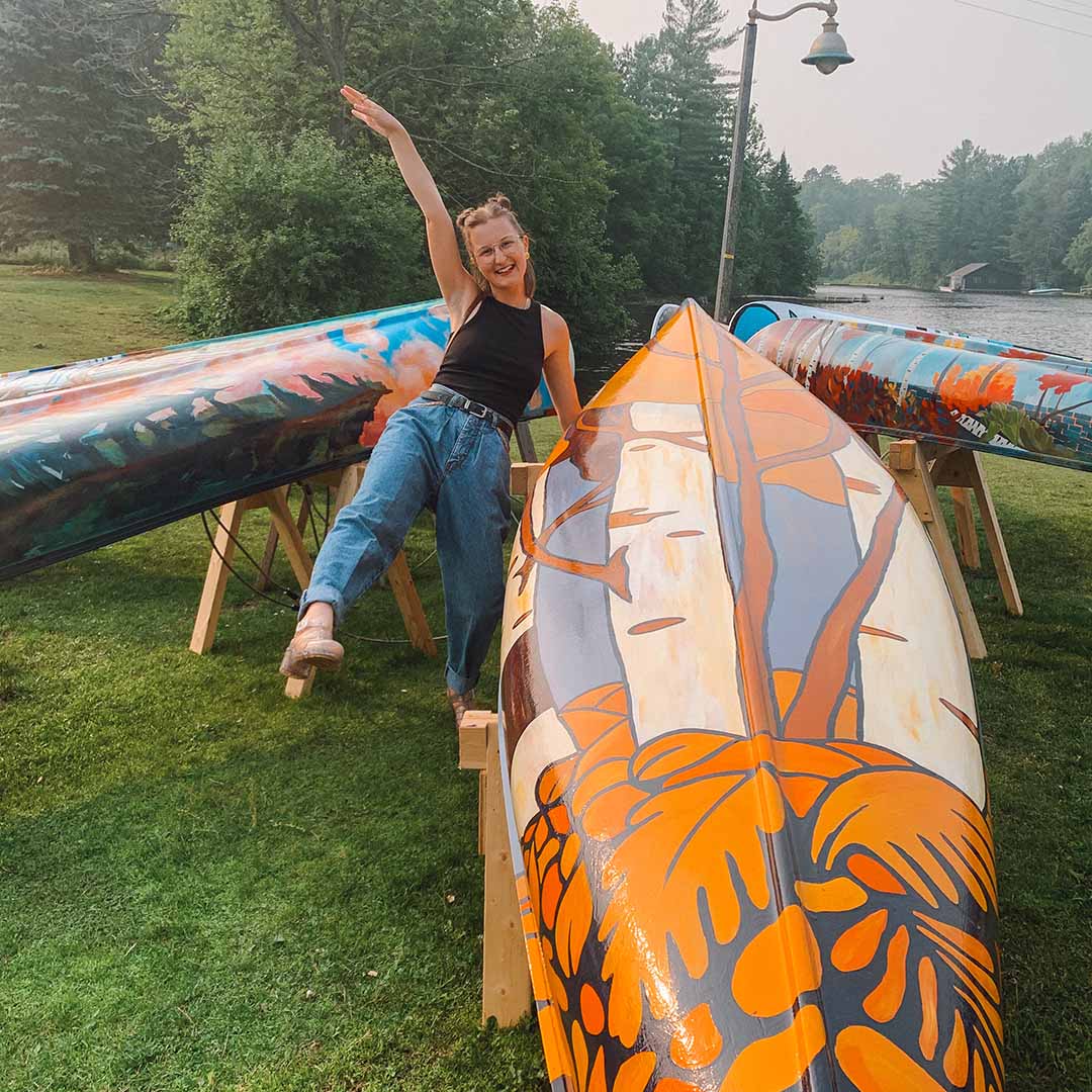 Taylor posing enthusiastically next to a colourful hand painted canoe
