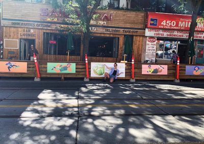 Artist posing in front of artwork displayed on the side of a patio in Toronto, ON